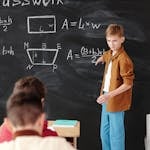 A young student explains math formulas on a blackboard during classwork.